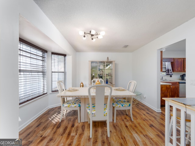 dining room featuring sink, a notable chandelier, light hardwood / wood-style flooring, and a textured ceiling