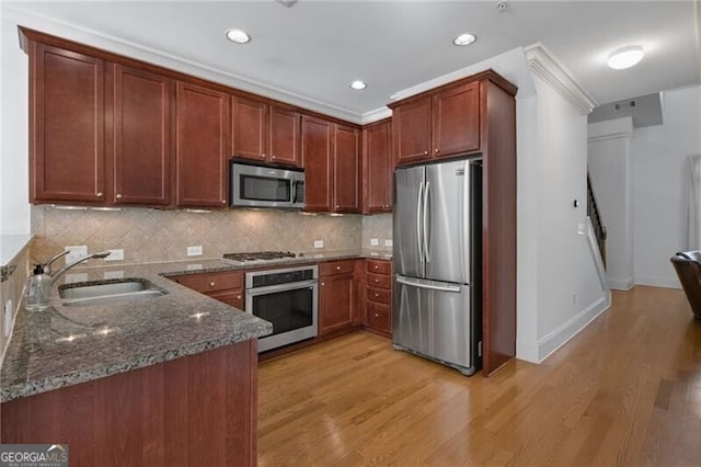 kitchen featuring sink, light hardwood / wood-style flooring, appliances with stainless steel finishes, dark stone counters, and backsplash