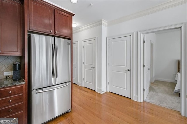 kitchen featuring light hardwood / wood-style floors, decorative backsplash, ornamental molding, and stainless steel refrigerator