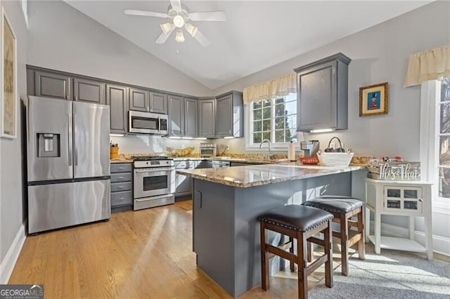 kitchen with lofted ceiling, stainless steel appliances, gray cabinets, and kitchen peninsula