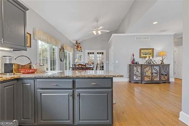 kitchen featuring light stone counters, gray cabinets, a healthy amount of sunlight, and light hardwood / wood-style flooring