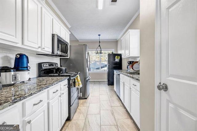 kitchen featuring appliances with stainless steel finishes, decorative light fixtures, dark stone countertops, white cabinets, and ornamental molding