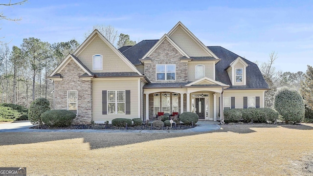 craftsman-style home with stone siding, a porch, and a front yard