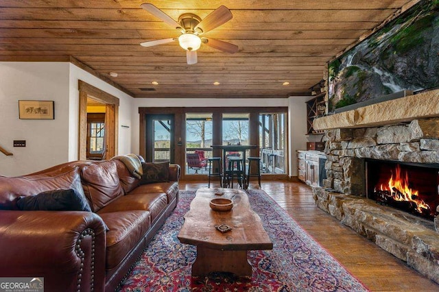 living room featuring ceiling fan, a stone fireplace, hardwood / wood-style floors, and wood ceiling