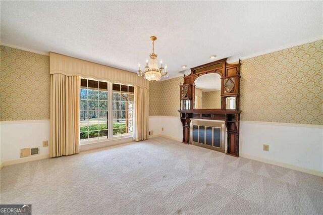 unfurnished living room with a fireplace, carpet floors, a notable chandelier, crown molding, and a textured ceiling