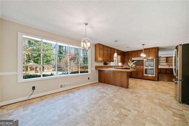 kitchen featuring an inviting chandelier, decorative light fixtures, a textured ceiling, kitchen peninsula, and stainless steel appliances