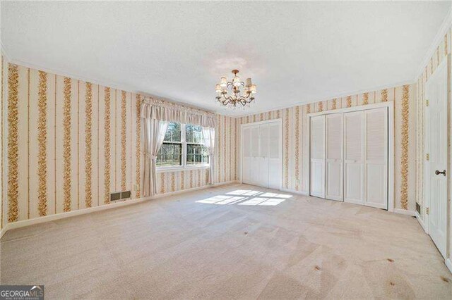 unfurnished bedroom with light colored carpet, a textured ceiling, and an inviting chandelier