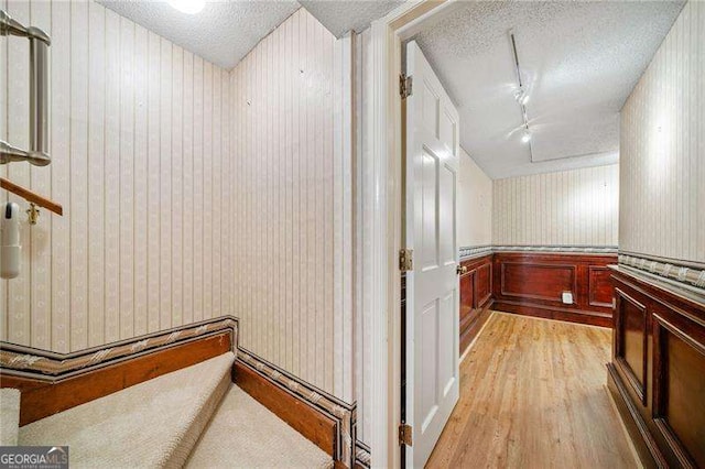 corridor featuring rail lighting, light hardwood / wood-style floors, and a textured ceiling