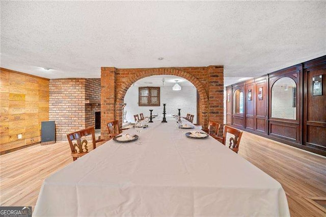 dining room featuring hardwood / wood-style flooring, a fireplace, a textured ceiling, and wood walls