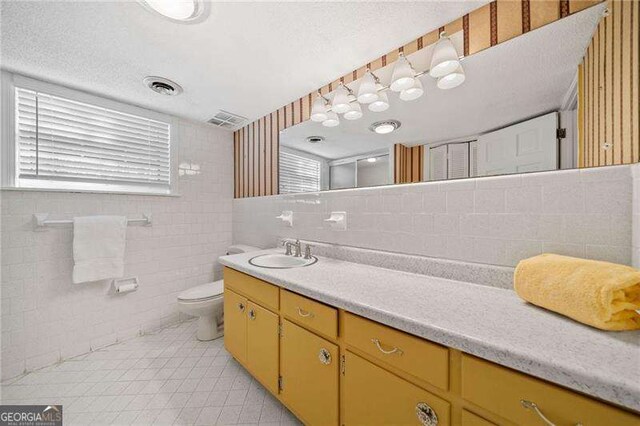 bathroom featuring tile walls, vanity, toilet, tile patterned floors, and a textured ceiling