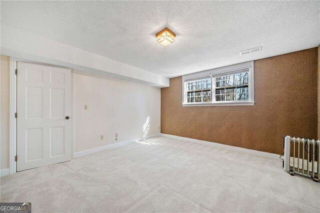 basement with light carpet, radiator, and a textured ceiling