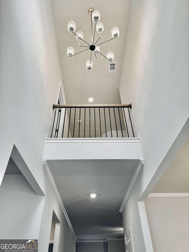 stairway with crown molding, an inviting chandelier, and a high ceiling