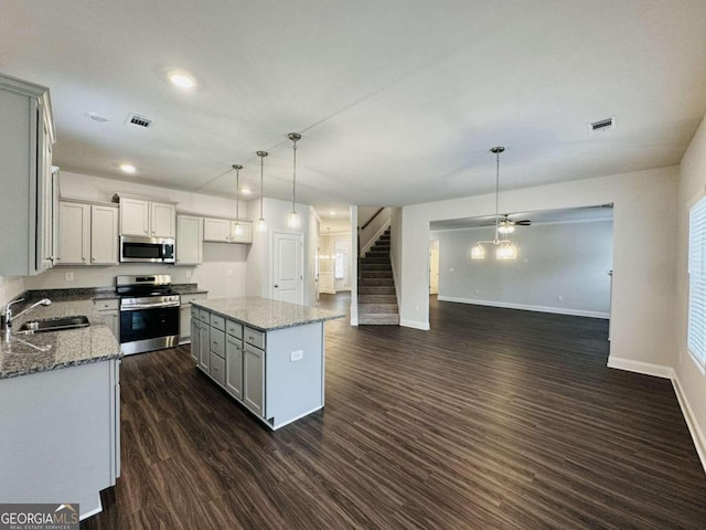 kitchen featuring pendant lighting, sink, appliances with stainless steel finishes, light stone counters, and a kitchen island