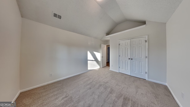 unfurnished bedroom with a closet, lofted ceiling, light carpet, and a textured ceiling