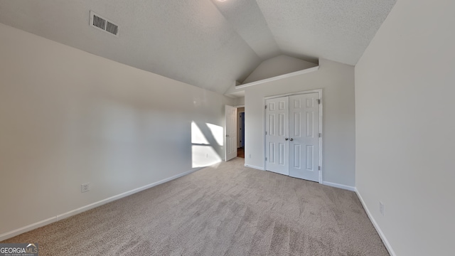 unfurnished bedroom featuring a closet, lofted ceiling, light carpet, and a textured ceiling