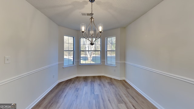 unfurnished dining area featuring an inviting chandelier, light hardwood / wood-style flooring, and a textured ceiling