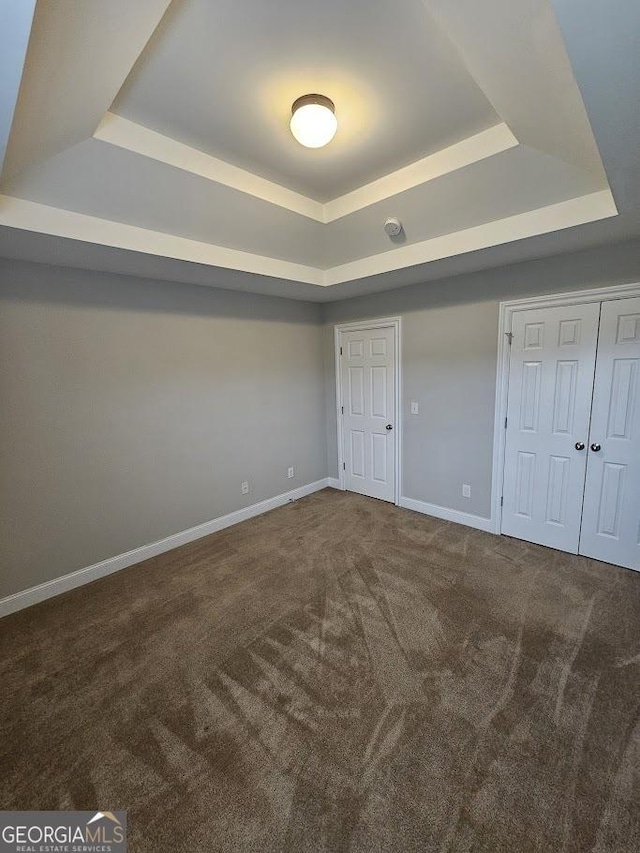 unfurnished bedroom with a closet, a raised ceiling, and carpet flooring