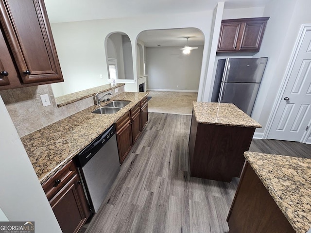 kitchen with sink, light hardwood / wood-style flooring, appliances with stainless steel finishes, a kitchen island, and light stone countertops