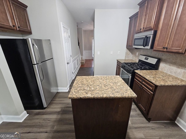 kitchen with dark wood-type flooring, a center island, appliances with stainless steel finishes, light stone countertops, and backsplash