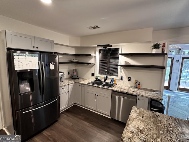 kitchen with sink, light stone counters, black fridge, dark hardwood / wood-style flooring, and stainless steel dishwasher