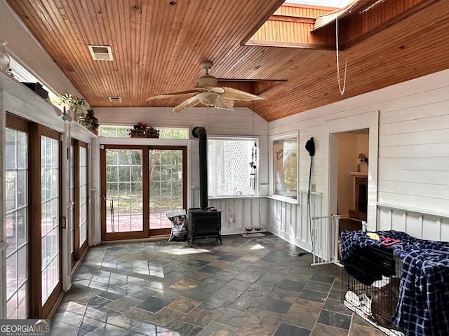 unfurnished sunroom with lofted ceiling with skylight, a wood stove, wooden ceiling, and ceiling fan