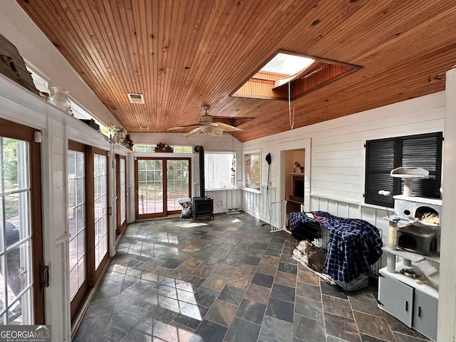 sunroom with wooden ceiling, plenty of natural light, lofted ceiling with skylight, and a wood stove