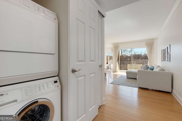 washroom with crown molding, stacked washer and dryer, and light hardwood / wood-style floors