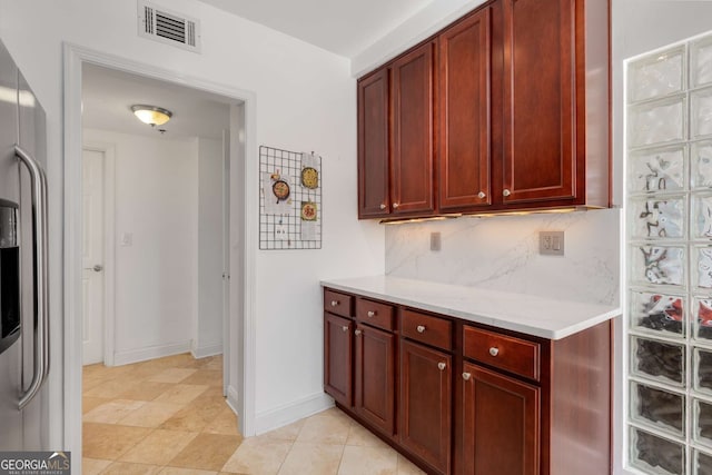 kitchen featuring tasteful backsplash, stainless steel refrigerator with ice dispenser, and light stone countertops