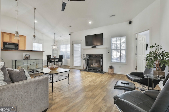 living room featuring high vaulted ceiling, a fireplace, and light hardwood / wood-style floors