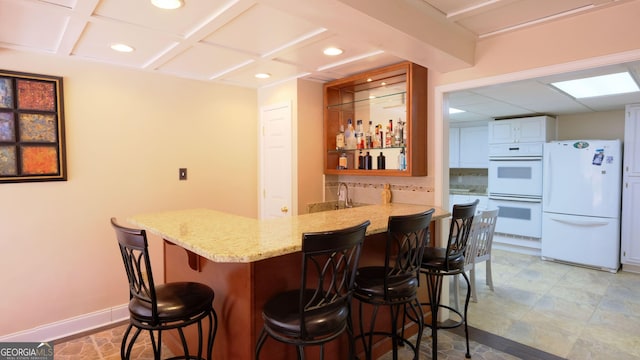 bar with sink, light stone counters, beamed ceiling, white appliances, and backsplash