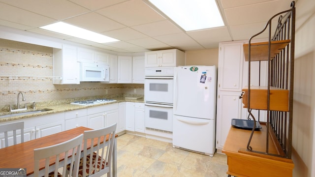 kitchen with white appliances, light stone countertops, sink, and white cabinets