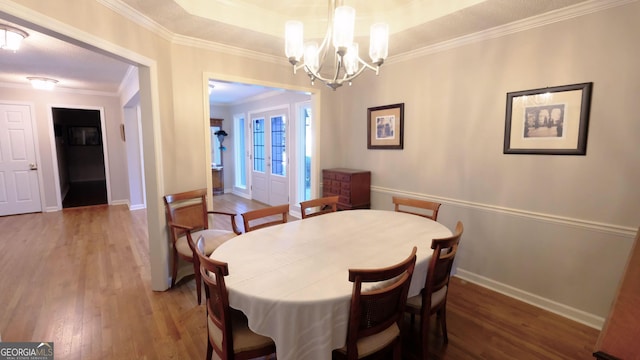 dining area with a raised ceiling, ornamental molding, an inviting chandelier, and dark hardwood / wood-style flooring