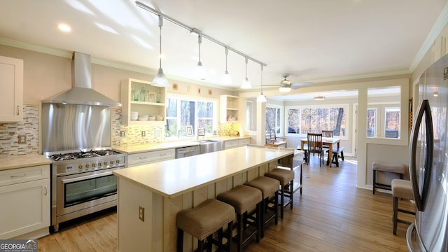 kitchen featuring white cabinetry, stainless steel appliances, a kitchen breakfast bar, a center island, and wall chimney exhaust hood