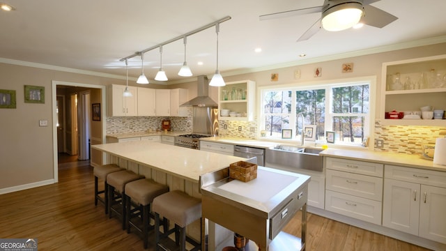 kitchen featuring white cabinetry, stainless steel appliances, a kitchen island, decorative light fixtures, and wall chimney exhaust hood