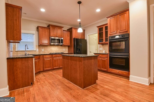 kitchen with sink, light wood-type flooring, a kitchen island, dark stone counters, and black appliances