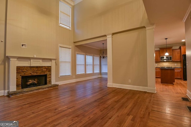 unfurnished living room with crown molding, an inviting chandelier, a towering ceiling, dark hardwood / wood-style floors, and a stone fireplace