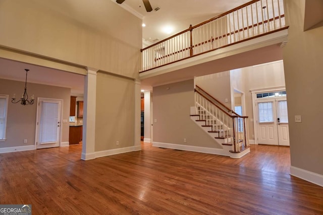 unfurnished living room featuring hardwood / wood-style flooring, ceiling fan with notable chandelier, and a high ceiling