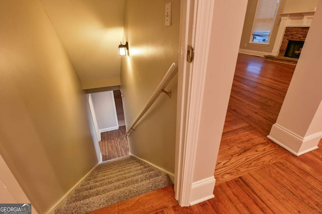 stairs featuring hardwood / wood-style flooring and a stone fireplace