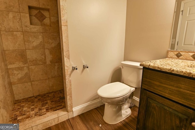 bathroom with toilet, tasteful backsplash, wood-type flooring, a tile shower, and vanity