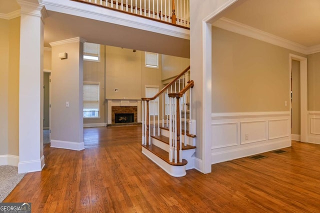 staircase featuring crown molding, decorative columns, a high ceiling, a fireplace, and wood-type flooring