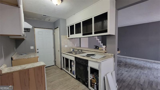 kitchen featuring sink, tasteful backsplash, black dishwasher, light hardwood / wood-style floors, and white cabinets