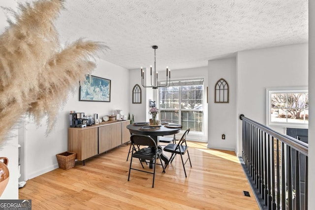 dining space with a notable chandelier, light hardwood / wood-style floors, and a textured ceiling