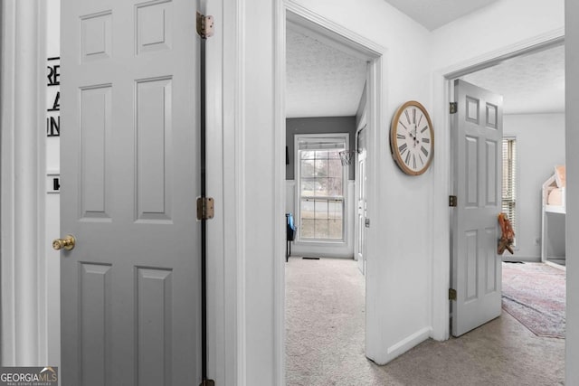 corridor with light colored carpet and a textured ceiling