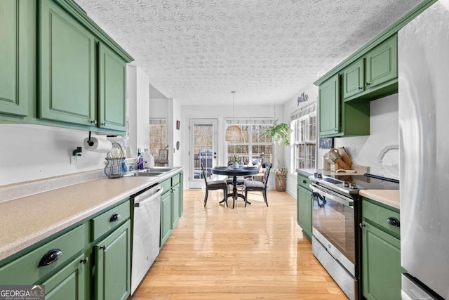 kitchen featuring sink, a textured ceiling, light wood-type flooring, green cabinets, and stainless steel appliances