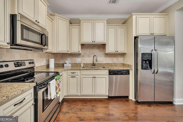 kitchen featuring sink, appliances with stainless steel finishes, ornamental molding, light stone countertops, and cream cabinets