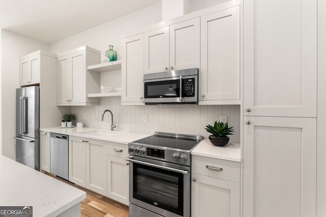 kitchen with sink, appliances with stainless steel finishes, white cabinetry, tasteful backsplash, and light stone countertops