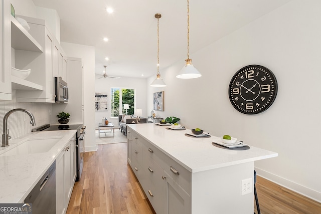 kitchen featuring appliances with stainless steel finishes, pendant lighting, sink, a center island, and light stone counters