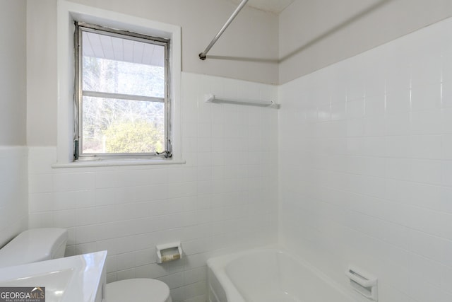 bathroom with bathtub / shower combination, toilet, and tile walls