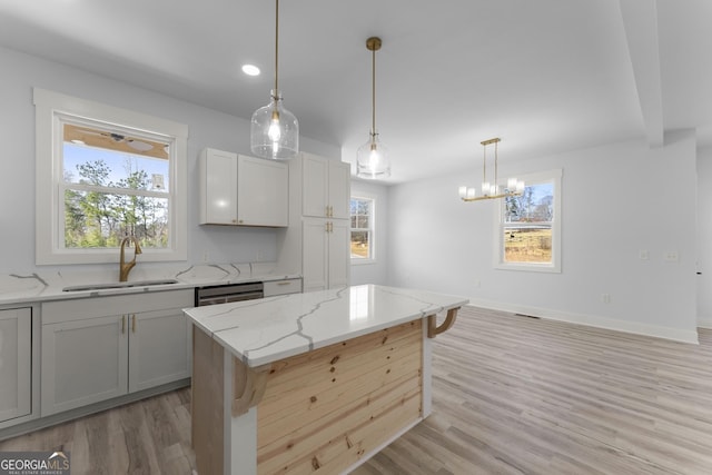 kitchen with a kitchen bar, sink, stainless steel dishwasher, a kitchen island, and light stone countertops