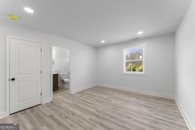 unfurnished bedroom with connected bathroom and light wood-type flooring